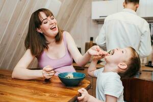 Mother with father feeding the child in the kitchen with pasta photo