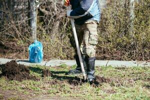 A man is planting a young tree. The farmer is digging the ground with a shovel for a small seedling. The concept of protection of the environment and ecology photo