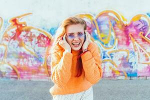 Portrait of a young laughing girl with braces listening to music in headphones in the summer on the street photo