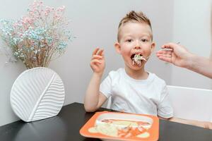 Happy child eating delicious pasta at the table in the kitchen photo