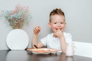 Laughing boy eats delicious pasta at the table in the kitchen photo