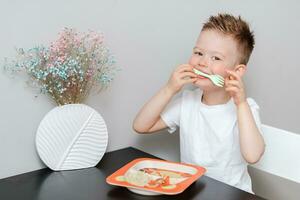 Happy child eating delicious pasta at the table in the kitchen photo