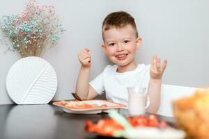 Laughing boy eats delicious pasta at the table in the kitchen photo