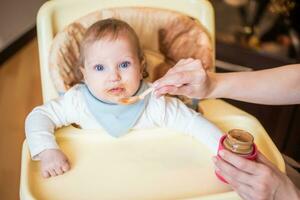 Mom feeds a happy baby fruit puree from a spoon. First food photo