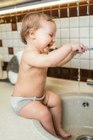 riendo pequeño niña toma higiene procedimientos en el lavabo en el cocina foto