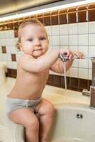 riendo pequeño niña toma higiene procedimientos en el lavabo en el cocina foto