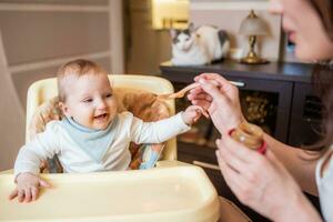 Mother feeds happy little daughter fruit puree from a spoon. First food photo