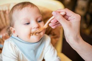 Mom feeds a happy baby fruit puree from a spoon. First food photo
