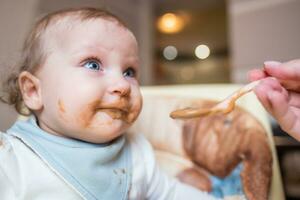 Happy mother feeding her cute little daughter fruit puree from a spoon. First food photo