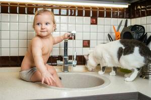 linda bebé jugando en el cocina lavabo con un gato foto