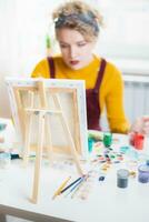 Woman sitting in front of a painting and painting with brushes on canvas at home photo