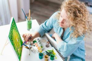 mujer sentado en frente de un pintura y pintura con cepillos en lona a hogar foto
