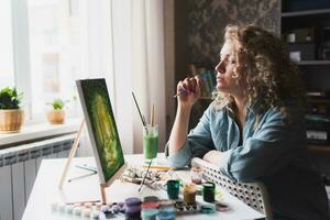 mujer sentado en frente de un pintura y pintura con cepillos en lona a hogar foto