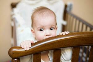 baby chewing on the crossbar of his crib photo