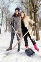 young women shoveling snow near a small wood photo