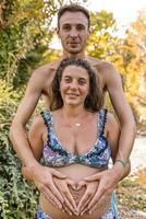 retrato de padres en trajes de baño formando corazón firmar con manos en embarazada mamá barriga foto