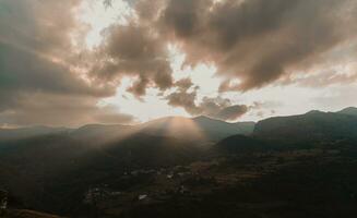 panoramic view of a valley surrounded by hills at sunset with the sun obscured by clouds photo