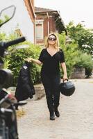 portrait of middle aged blonde female biker taking a break near her powerful black motorbike photo