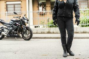 maduro mujer en ropa de un motociclista estar en frente de un moderno motocicleta en el la carretera foto