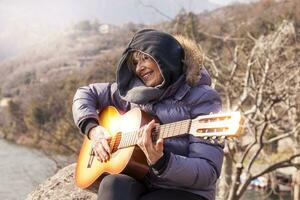 beautiful mature woman playing a guitar sitting on a rock photo