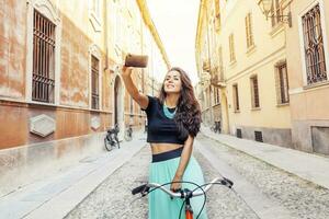 bonito joven niña con un bicicleta toma un selfie alrededor pueblo foto