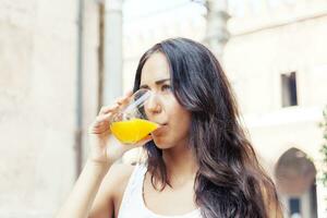 retrato de atractivo niña mientras Bebiendo un naranja jugo foto