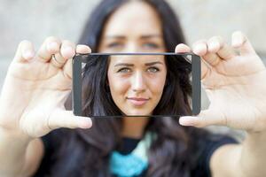 bonito mujer con gris ojos tomar un selfie con inteligente teléfono foto