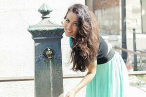 portrait of pretty girl drinks water from source in summer city photo