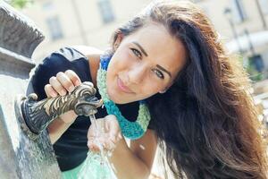 retrato de bonito niña bebidas agua desde fuente en verano ciudad foto