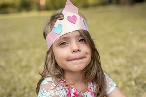 retrato de linda niña con un papel corona sentado en un público parque foto