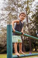 sonriente linda niño alpinismo en un metal barandilla en un público parque foto