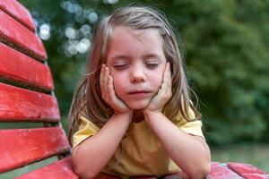 portrait of little cute girl with closed eyes leaning with elbows on a red bench photo