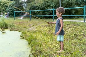 pequeño sonriente niño jugando con un palo por un estanque en un público parque foto