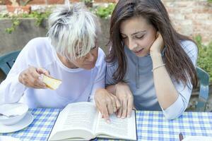 pretty mom and daughter reading a book while having breakfast outdoors photo