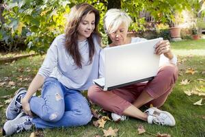 pretty mom and daughter consult the laptop under a tree in autumn photo