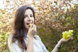 young beautiful girl sitting under a tree eating grapes photo