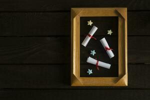 Flat lay romantic background. Giftbox, rolled wish papers, and wooden frame with paper hearts on dark wood board. photo