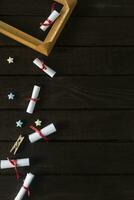 Flat lay romantic background. Giftbox, rolled wish papers, and wooden frame with paper hearts on dark wood board. photo