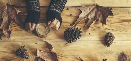 taza de té en hembra manos. otoño hojas terminado de madera mesa. otoño todavía vida concepto. caer, otoño comida y beber. parte superior vista. foto