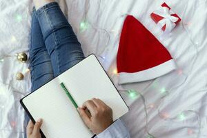 High angle view to young woman lying in bed and writing with pen on notebook. Wintertime. Christmas holidays. A woman making plans for the new year photo