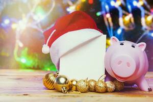 Buying, shopping Xmas gifts, presents. Depositing money for Xmas holidays. Seasonal winter festive spendings concept. Piggybank, Xmas decorations and blank card on wood photo