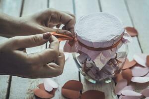 Lover's day. Hand opening glass jar or date Jar with desires. Red paper hearts at background. photo