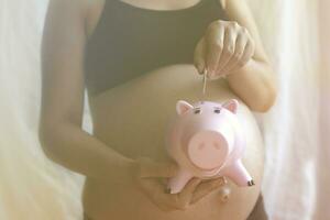 embarazada mujer poniendo dinero dentro cerdito banco foto