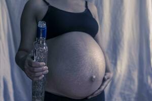 Pregnant woman holding vodka alcohol bottle photo