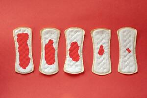 Feminine hygiene pads with blood during period days on red background photo