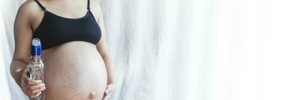 Pregnant woman holding vodka alcohol bottle photo