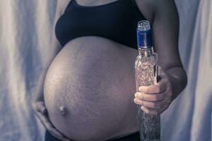 Pregnant woman holding vodka alcohol bottle photo