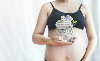 Pregnant women holding shopping cart with baby shoes. Pregnancy shopping item for children concept photo