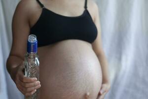 Pregnant woman holding vodka alcohol bottle photo