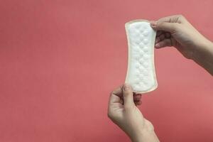 A white sanitary pad in woman's hands on a pink background with copy space. Absorbent item for women special days. Hygiene and health concept. photo